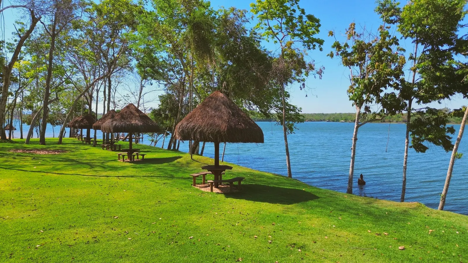 Quiosques de palha com mesas no gramado da margem do Quinta do Lago, à beira da água